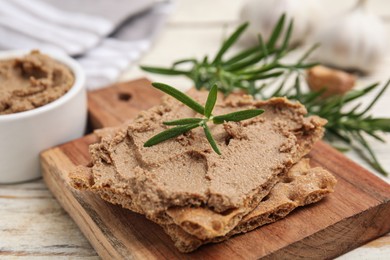 Photo of Crispy crackers with delicious meat pate and rosemary on white wooden table, closeup