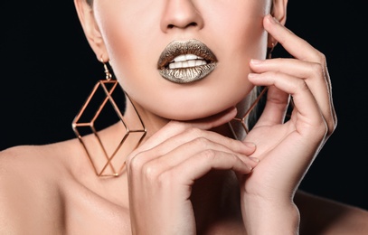 Photo of Beautiful lady with gold lipstick on black background, closeup