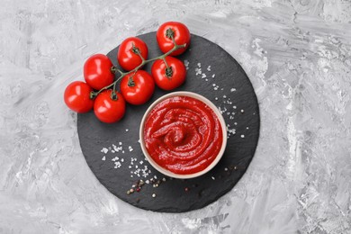 Photo of Organic ketchup in bowl, fresh tomatoes and spices on grey textured table, top view. Tomato sauce