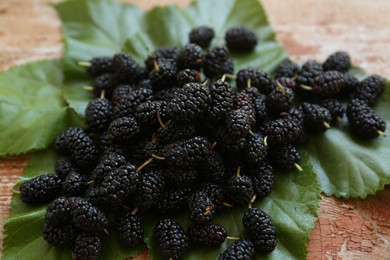 Photo of Heap of delicious ripe black mulberries and green leaves on wooden table, closeup