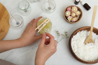 Photo of Woman decorating homemade candle with gypsophila flowers at table, above view