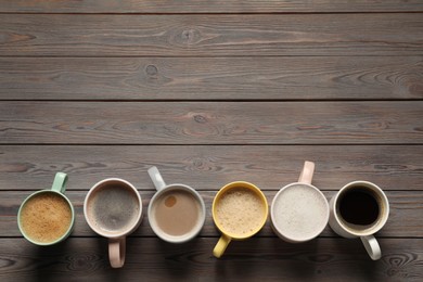 Photo of Many different cups with aromatic coffee on wooden table, flat lay. Space for text