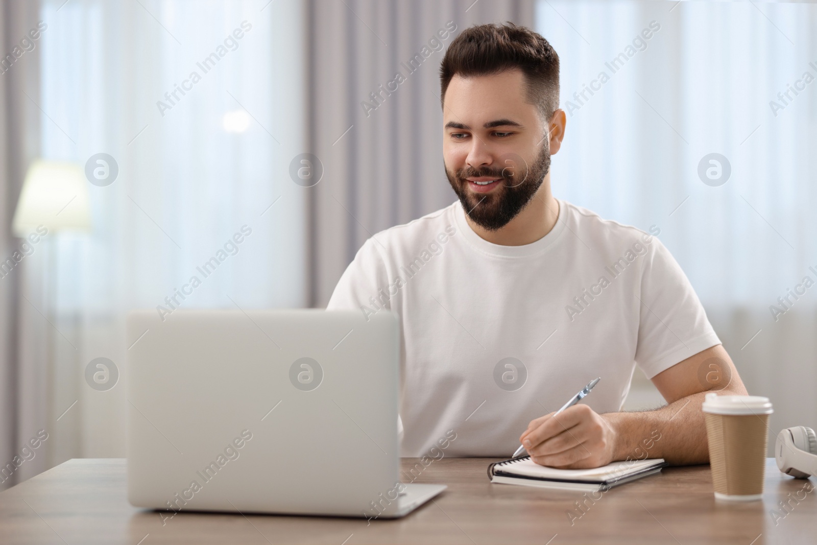 Photo of Young man watching webinar at table in room