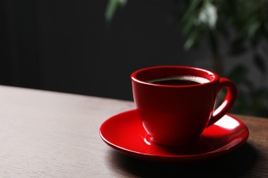 Photo of Red cup with aromatic coffee on wooden table indoors. Space for text
