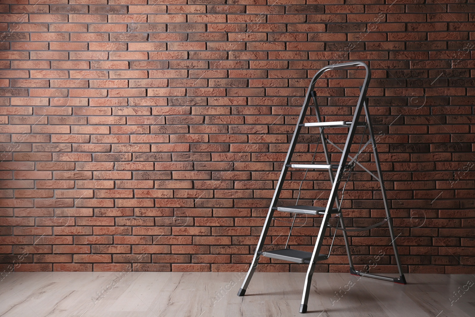 Photo of Modern metal stepladder near brick wall indoors. Space for text