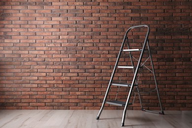 Photo of Modern metal stepladder near brick wall indoors. Space for text