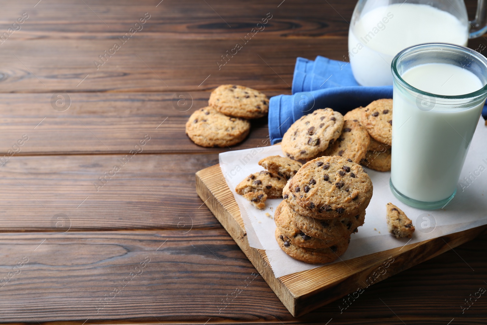 Photo of Delicious chocolate chip cookies and glass of milk on wooden table, space for text