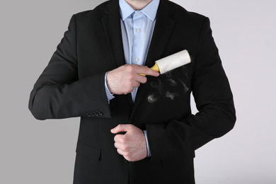 Photo of Man removing hair from black jacket with lint roller on  light grey background, closeup