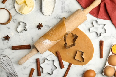 Rolling pin, dough, different cutters and ingredients for Christmas cookies on white marble table, flat lay