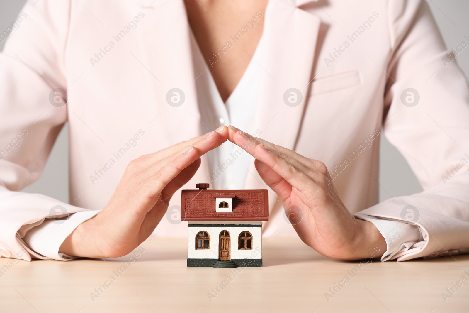 Photo of Female agent covering house model at table, closeup. Home insurance