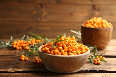 Photo of Fresh ripe sea buckthorn in bowl on wooden table. Space for text