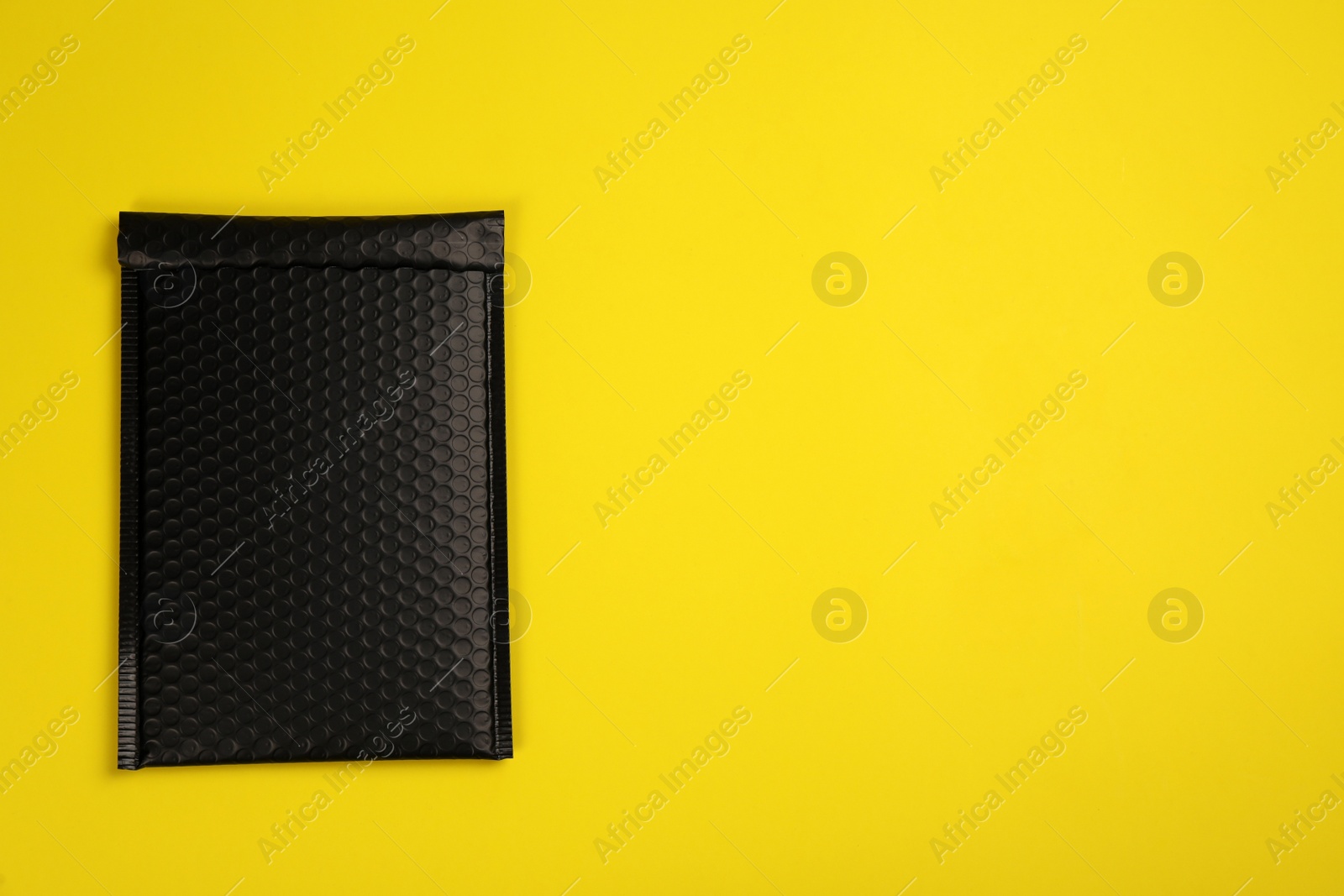 Photo of Padded envelope with bubble wrap on yellow background, top view. Space for text