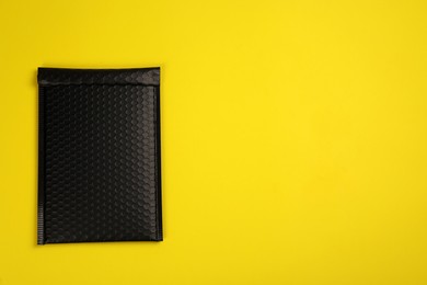 Photo of Padded envelope with bubble wrap on yellow background, top view. Space for text