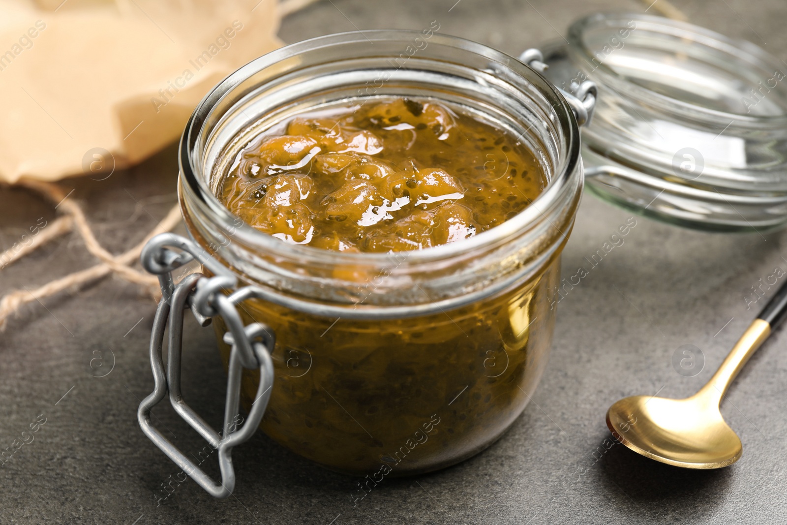 Photo of Jar of delicious gooseberry jam on grey table, closeup