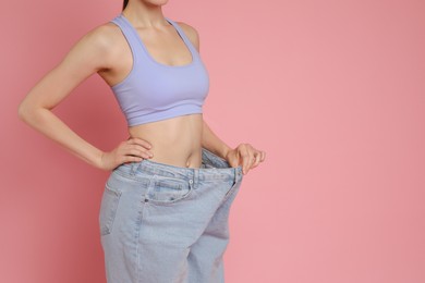 Woman in big jeans showing her slim body on pink background, closeup. Space for text