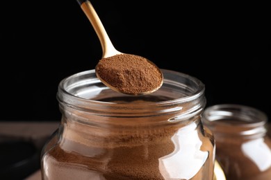 Photo of Spoon of instant coffee over jar against black background, closeup