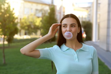 Photo of Beautiful woman blowing gum in park, space for text
