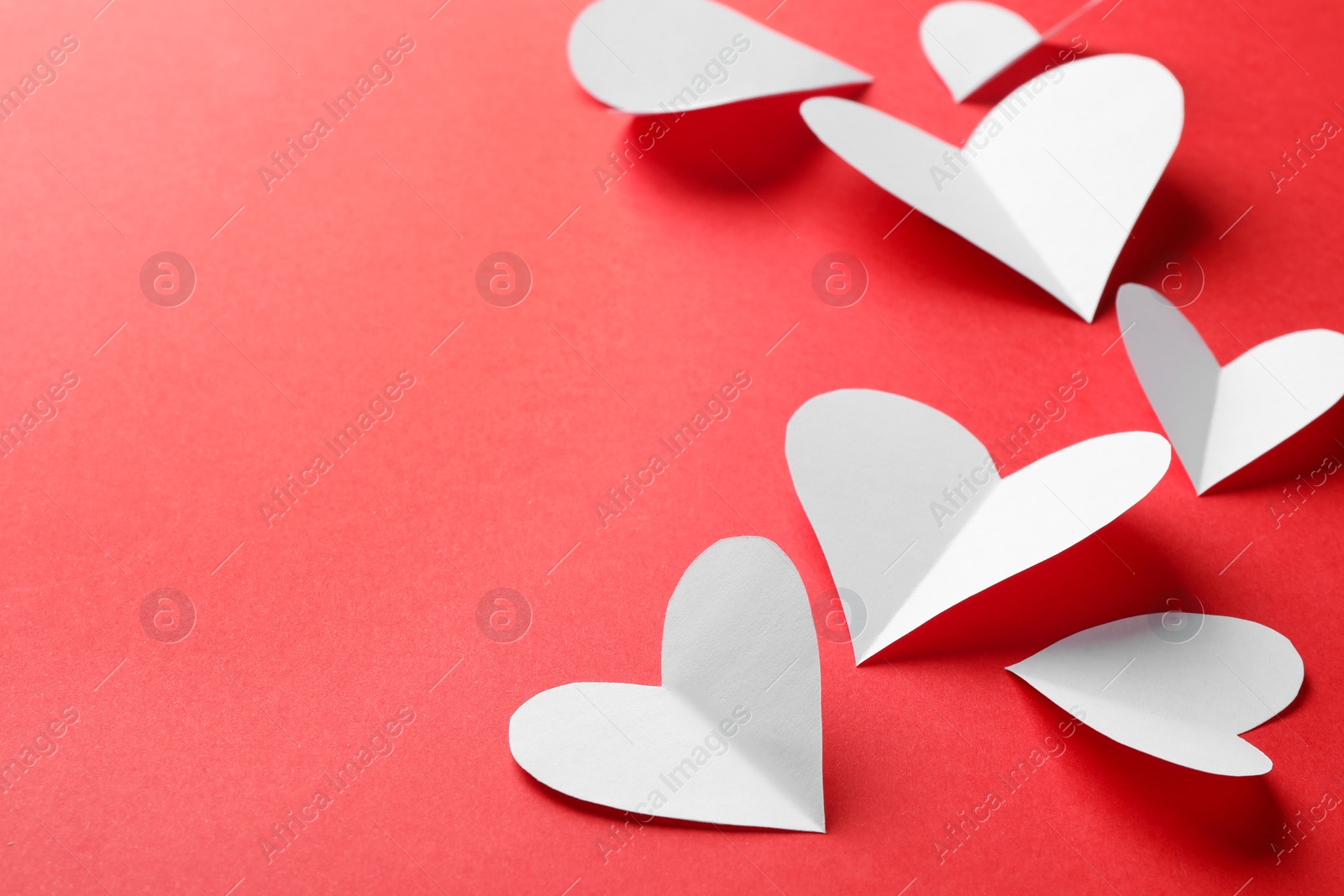 Photo of White paper hearts on red background. Space for text