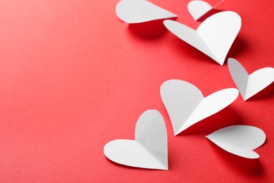 White paper hearts on red background. Space for text