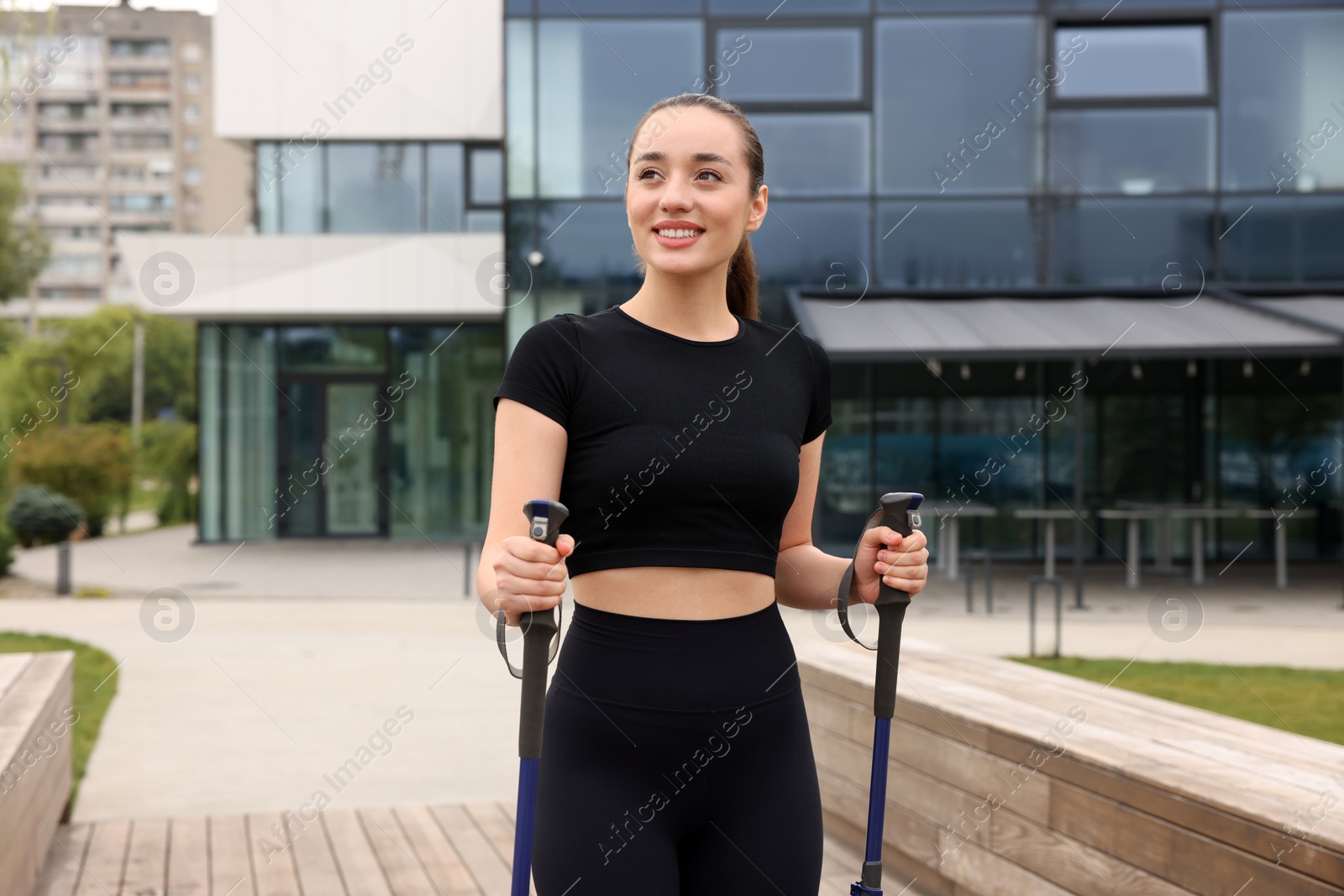 Photo of Young woman practicing Nordic walking with poles outdoors