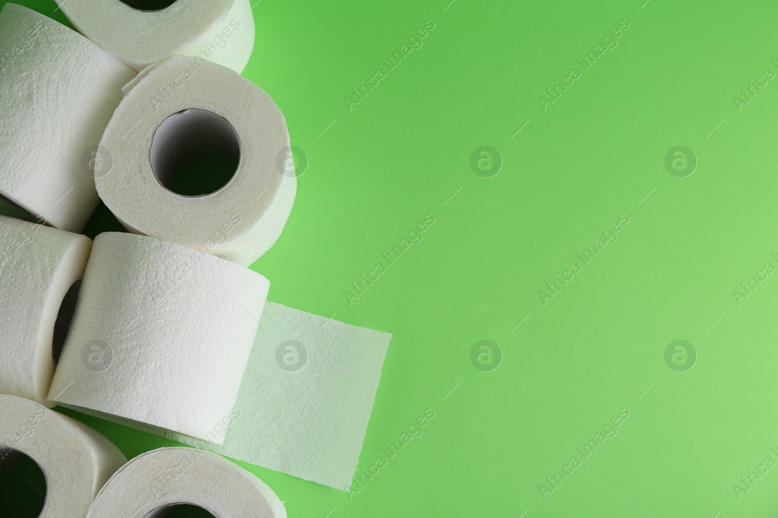 Photo of Soft toilet paper rolls on green background, flat lay. Space for text