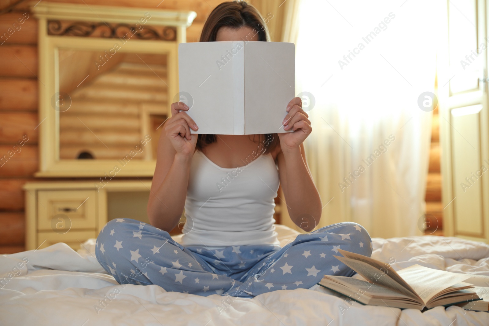 Photo of Young woman holding book on bed at home