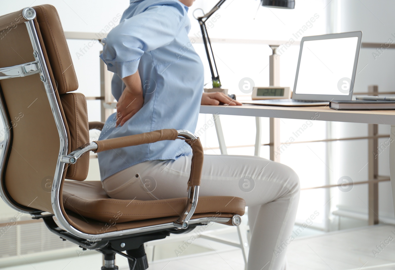 Photo of Woman suffering from back pain at workplace in office, closeup