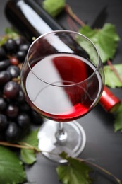 Photo of Glass and bottle of red wine and fresh ripe juicy grapes on table