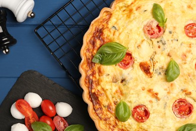 Photo of Delicious quiche with mozzarella cheese, tomatoes and basil on blue wooden table, flat lay