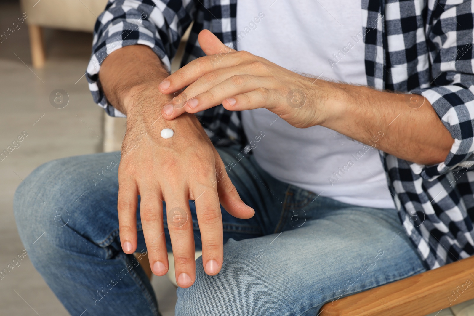 Photo of Man applying cream onto hand indoors, closeup