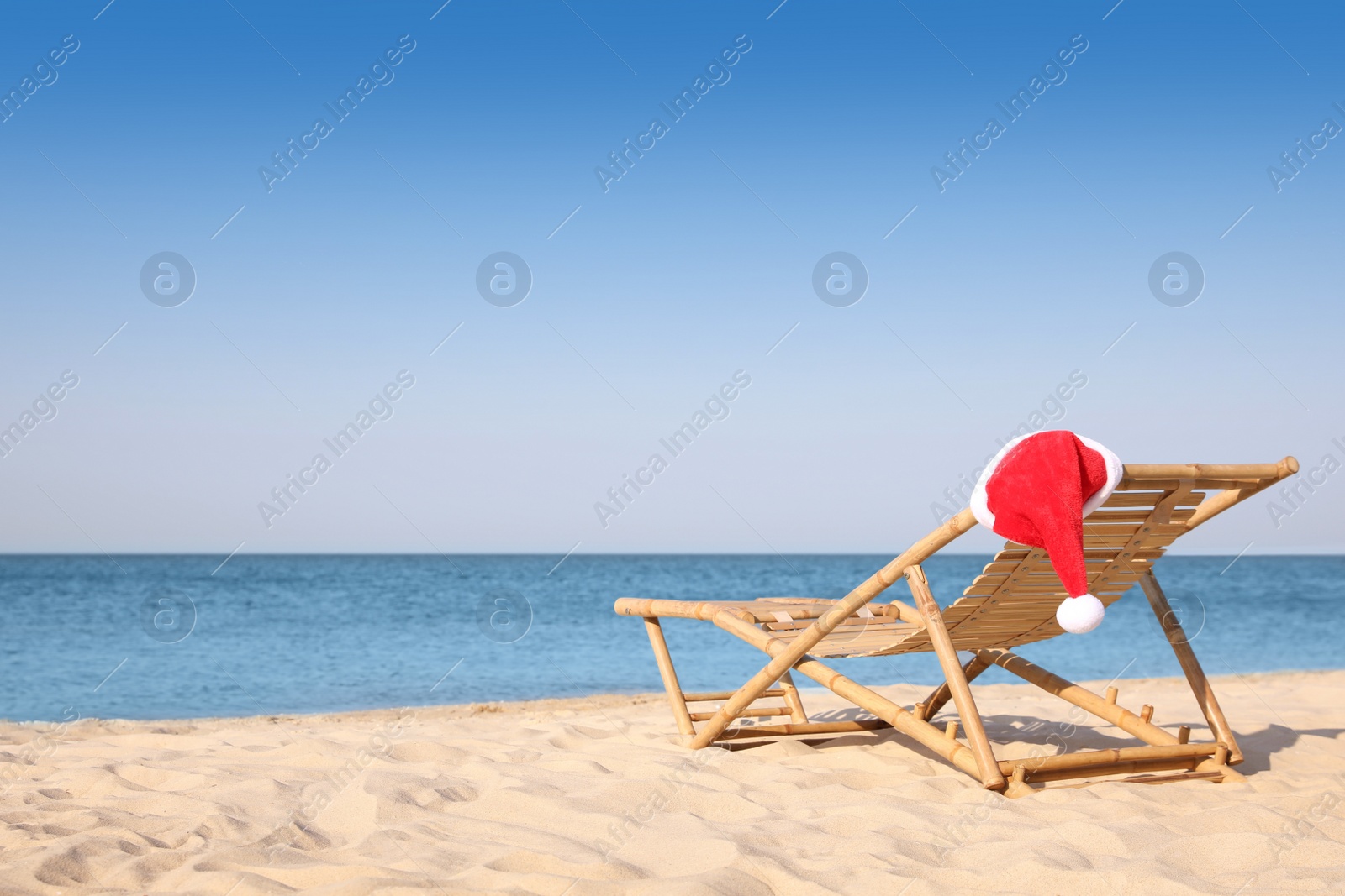 Photo of Sun lounger with Santa's hat on beach, space for text. Christmas vacation