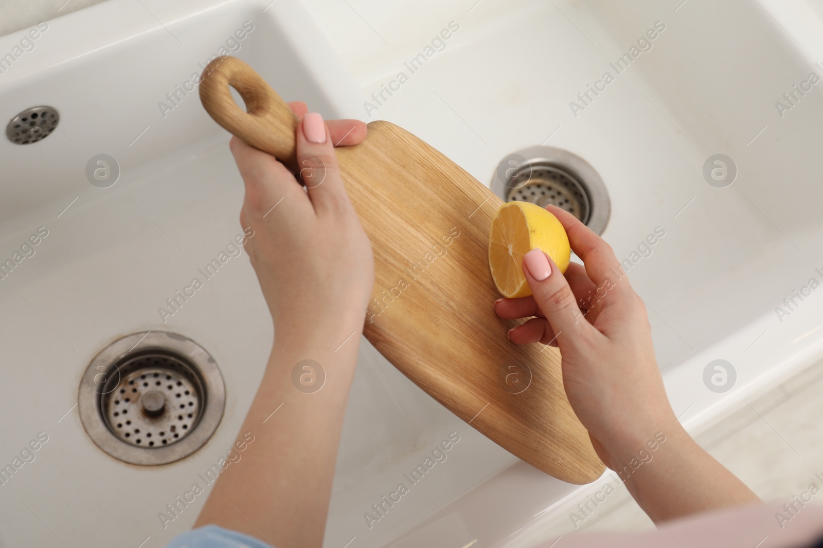 Photo of Woman rubbing wooden cutting board with lemon at sink in kitchen, closeup