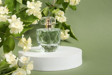 Photo of Presentation of aromatic perfume in bottle and beautiful jasmine flowers against pale green background, space for text