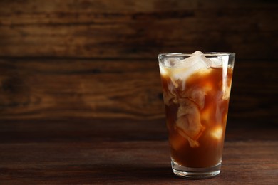 Glass of coffee with milk and ice cubes on wooden table. Space for text