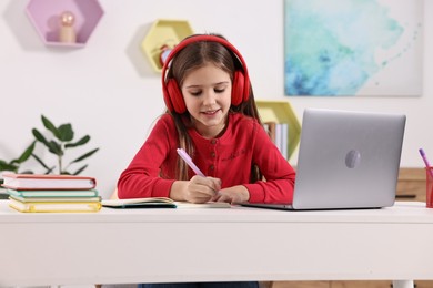 E-learning. Cute girl taking notes during online lesson at table indoors