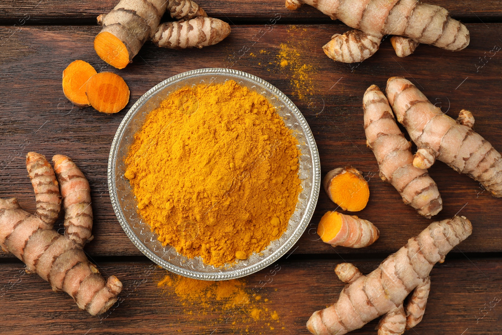 Photo of Plate with aromatic turmeric powder and cut roots on wooden table, flat lay