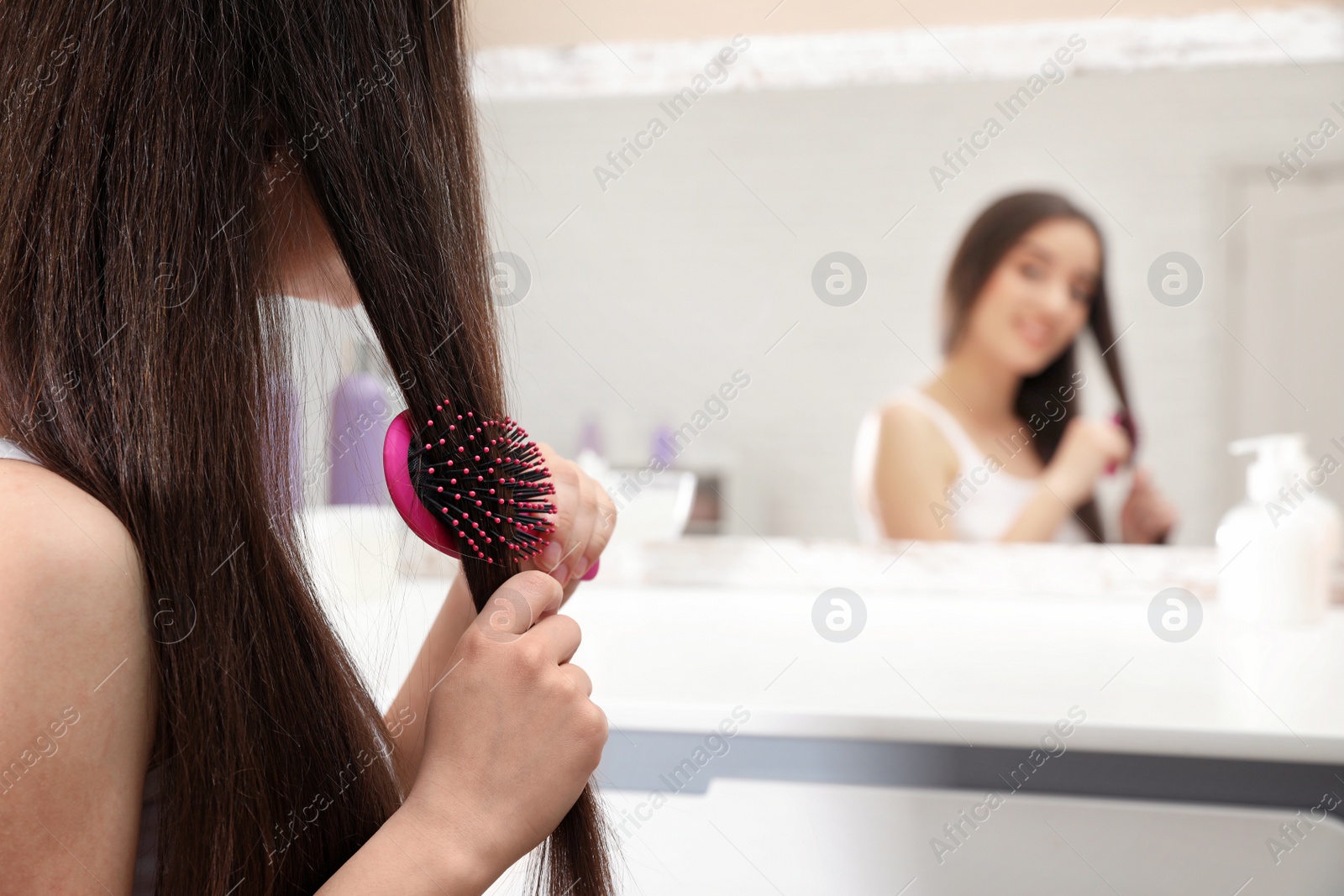 Photo of Beautiful young woman with hair brush near mirror in bathroom