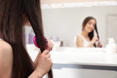 Beautiful young woman with hair brush near mirror in bathroom