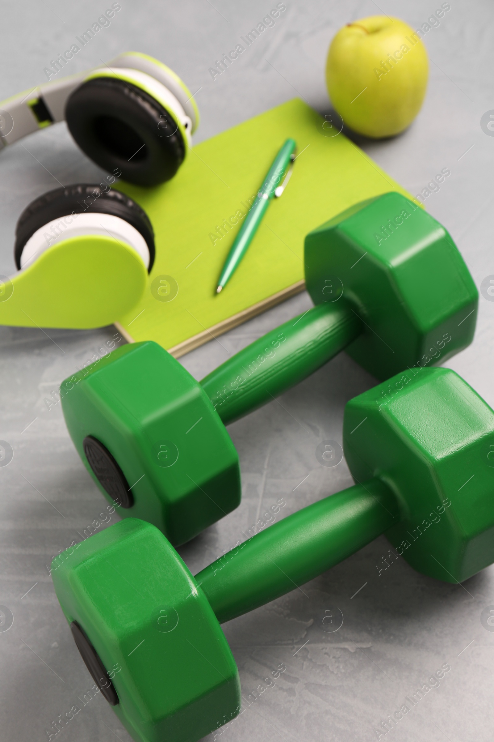 Photo of Dumbbells, headphones, apple and stationery on light grey table, closeup