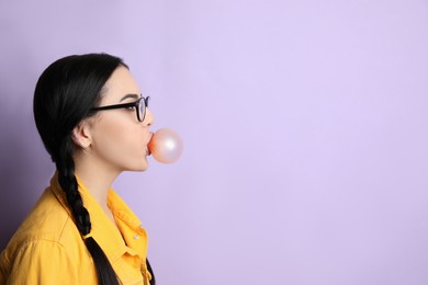 Fashionable young woman with braids blowing bubblegum on lilac background, space for text