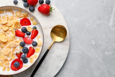 Bowl of tasty crispy corn flakes with milk and berries on light grey table, top view. Space for text