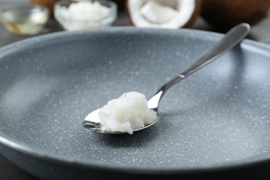 Frying pan with organic coconut cooking oil and spoon on table, closeup