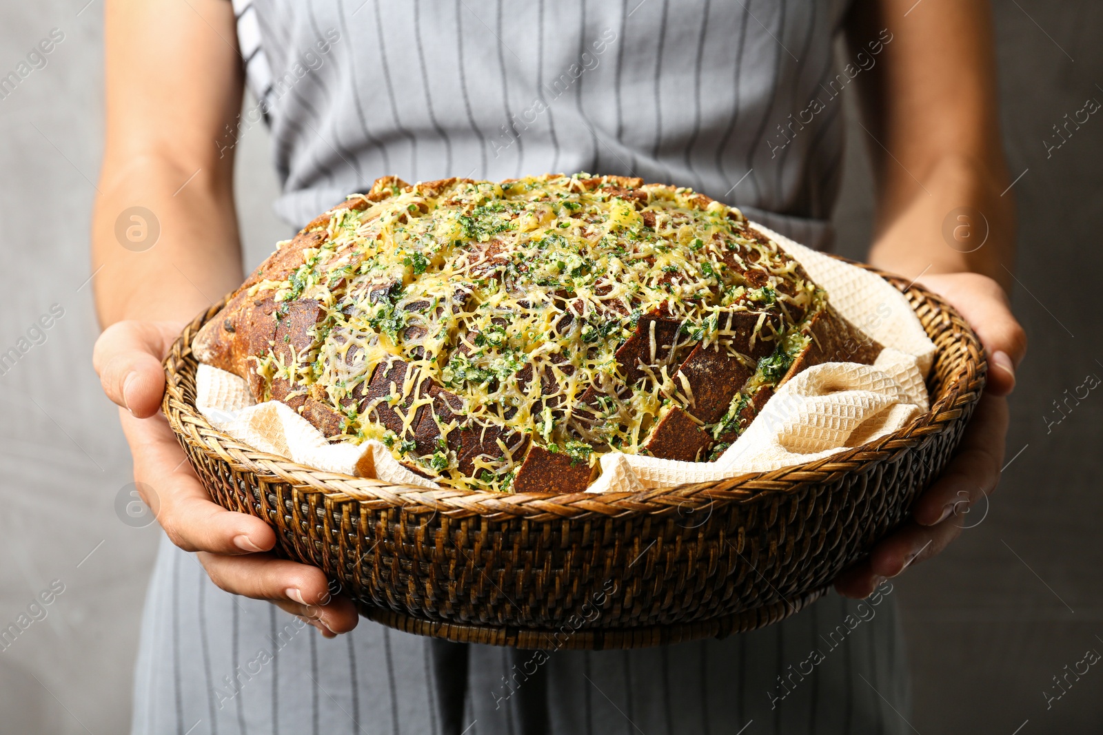 Photo of Woman holding tasty homemade garlic bread with cheese and herbs against grey background, closeup