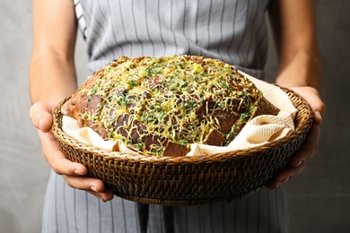 Photo of Woman holding tasty homemade garlic bread with cheese and herbs against grey background, closeup