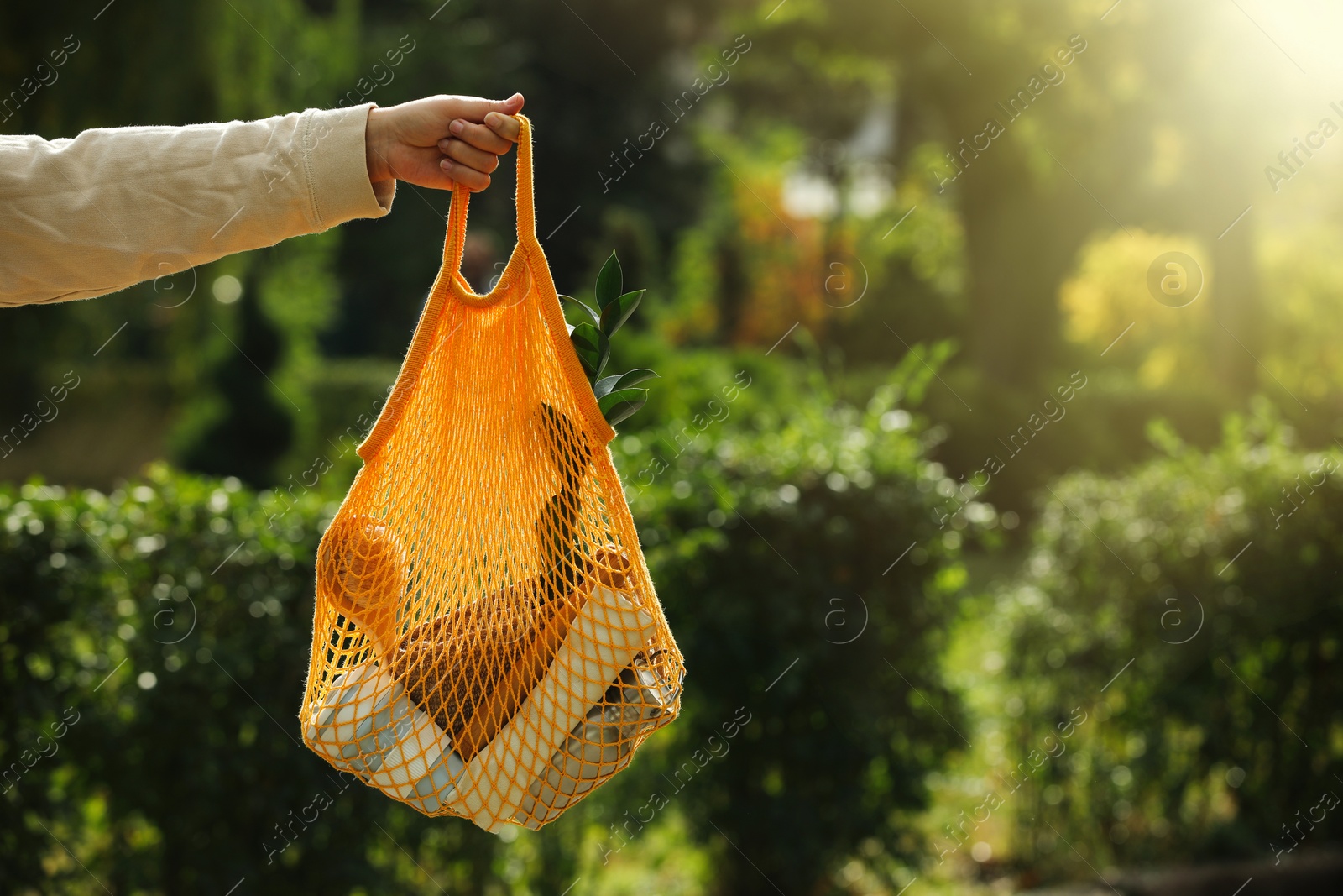 Photo of Conscious consumption. Woman with net bag of eco friendly products outdoors, closeup. Space for text