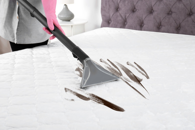 Woman disinfecting mattress with vacuum cleaner, closeup