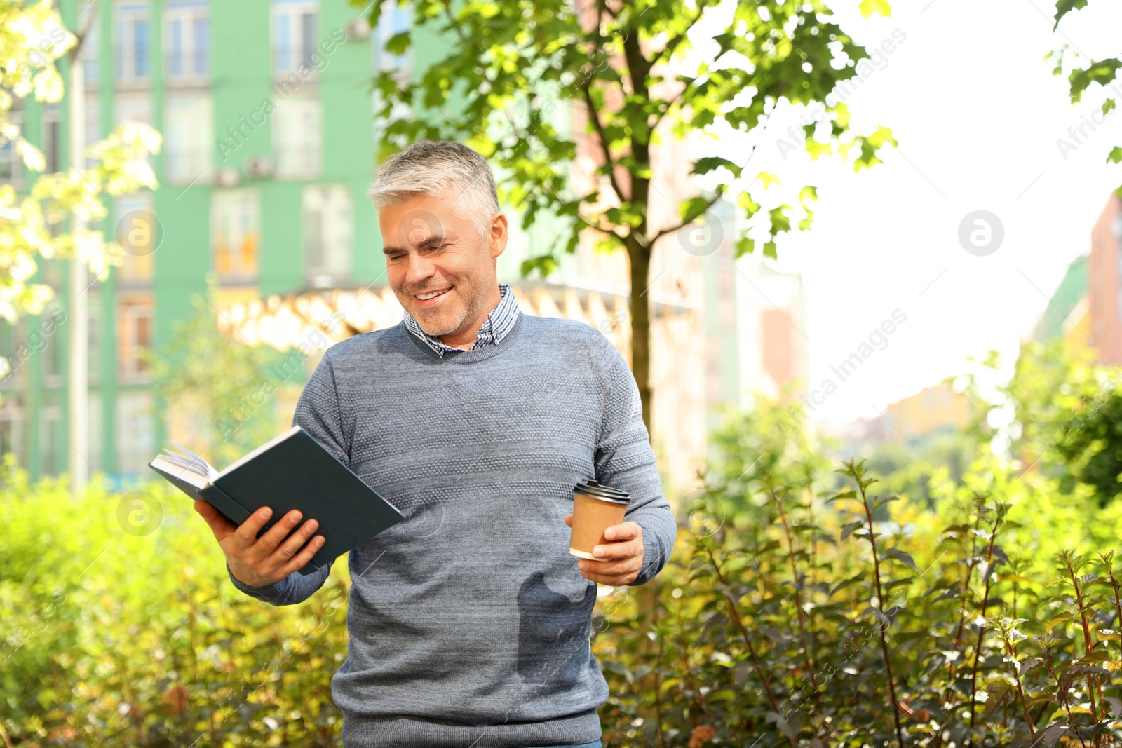 Photo of Handsome mature man with coffee and book in park. Space for text