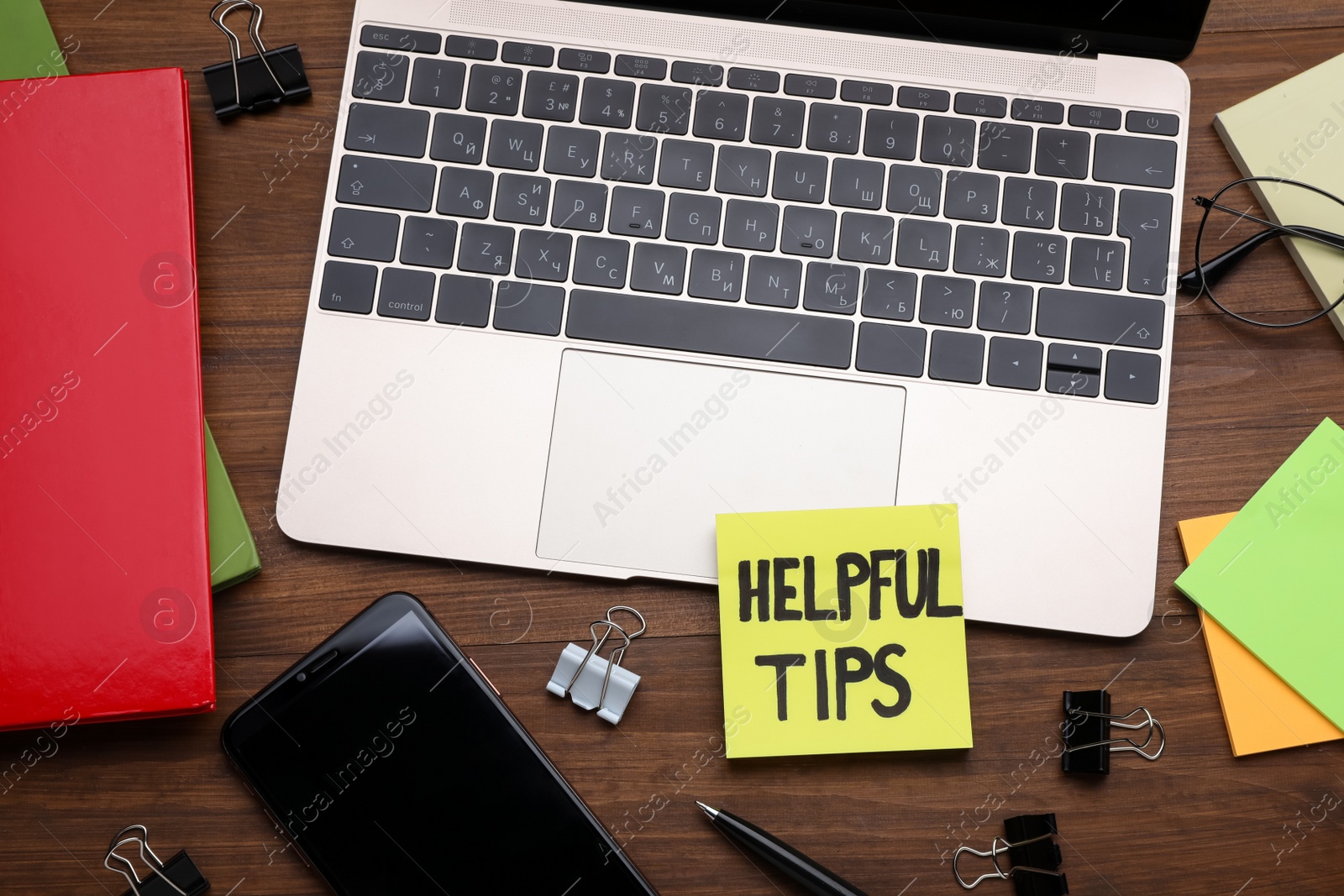 Photo of Paper note with phrase Helpful Tips, laptop, mobile phone and stationery on wooden table, flat lay