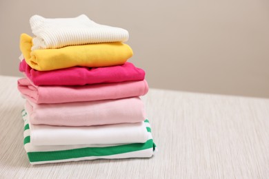 Photo of Stack of folded clothes on wooden table against beige background, space for text