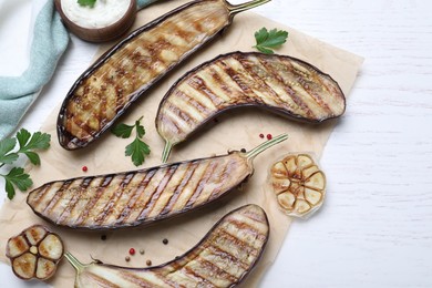 Photo of Delicious grilled eggplant halves and sauce on white wooden table, flat lay